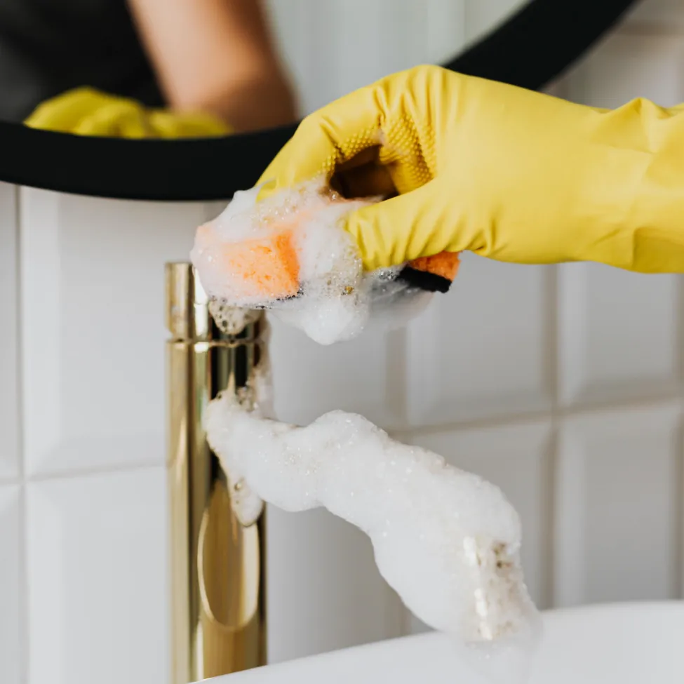 A person wearing yellow gloves cleaning the sink.