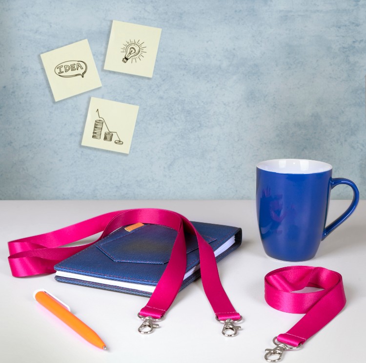 A blue mug, notebook and pink lanyard on a table.