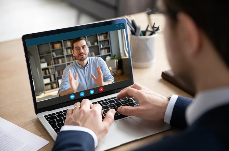 A man on his laptop with another person in the background.